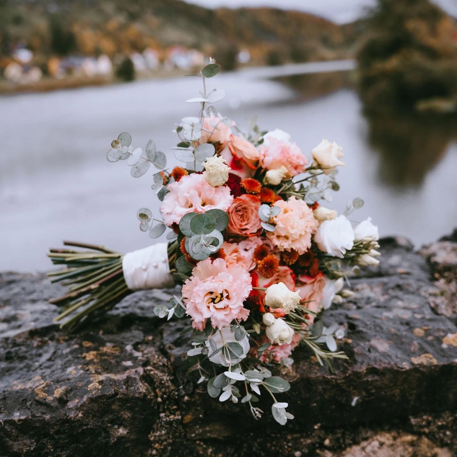 Rosa-weißer Brautstrauß auf einer Steinmauer am Fluss