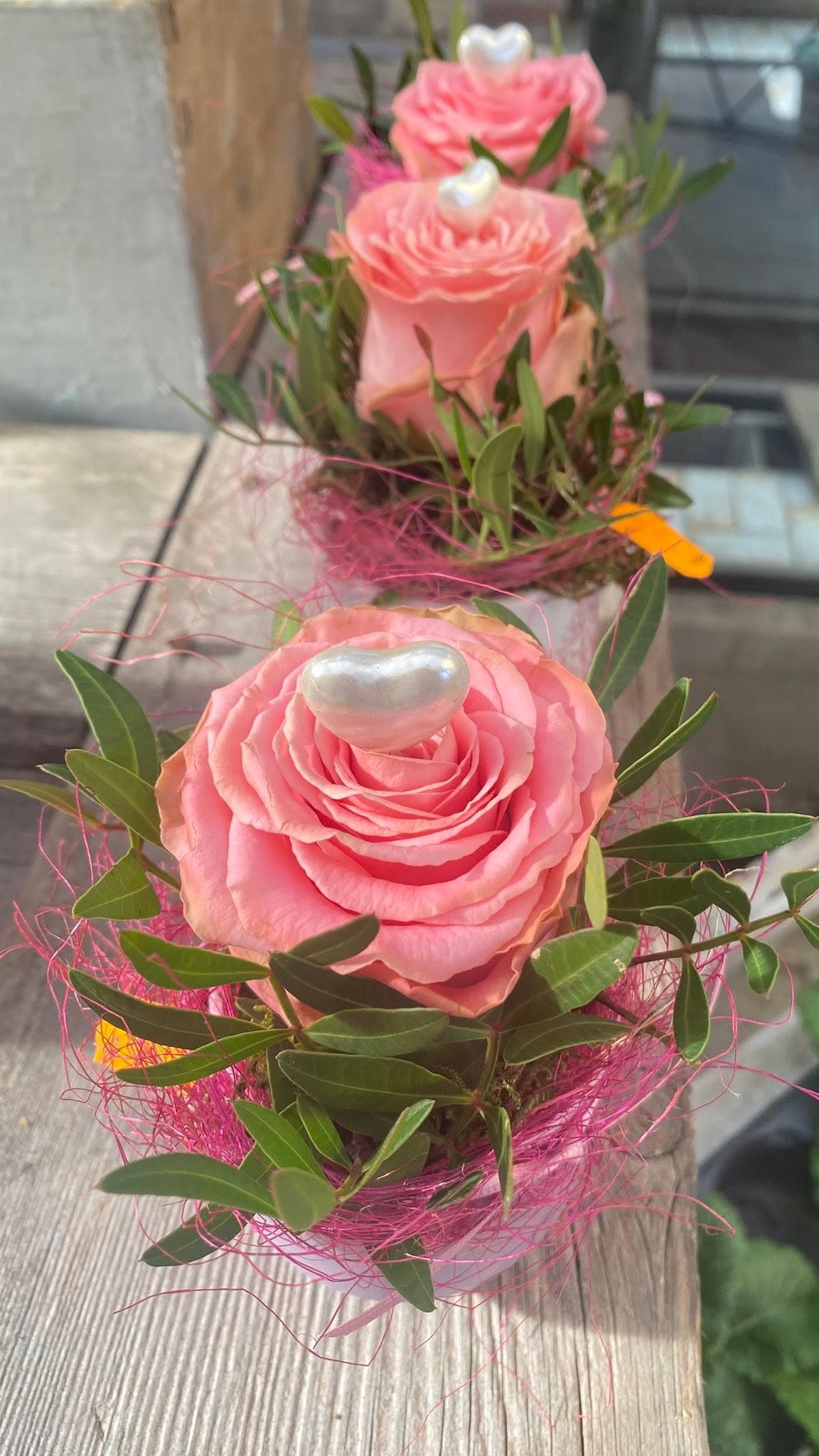 Drei kleine Gestecke mit rosa Rosen und Perlenherzen im Sonnenlicht