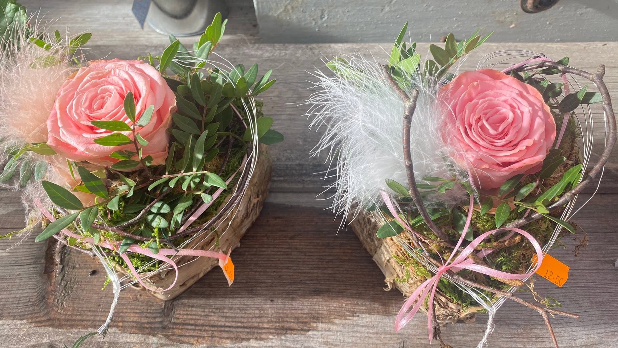 Zwei kleine Tischdekorationen mit rosa Rose, Feder und Zweigherz auf Holzscheiben