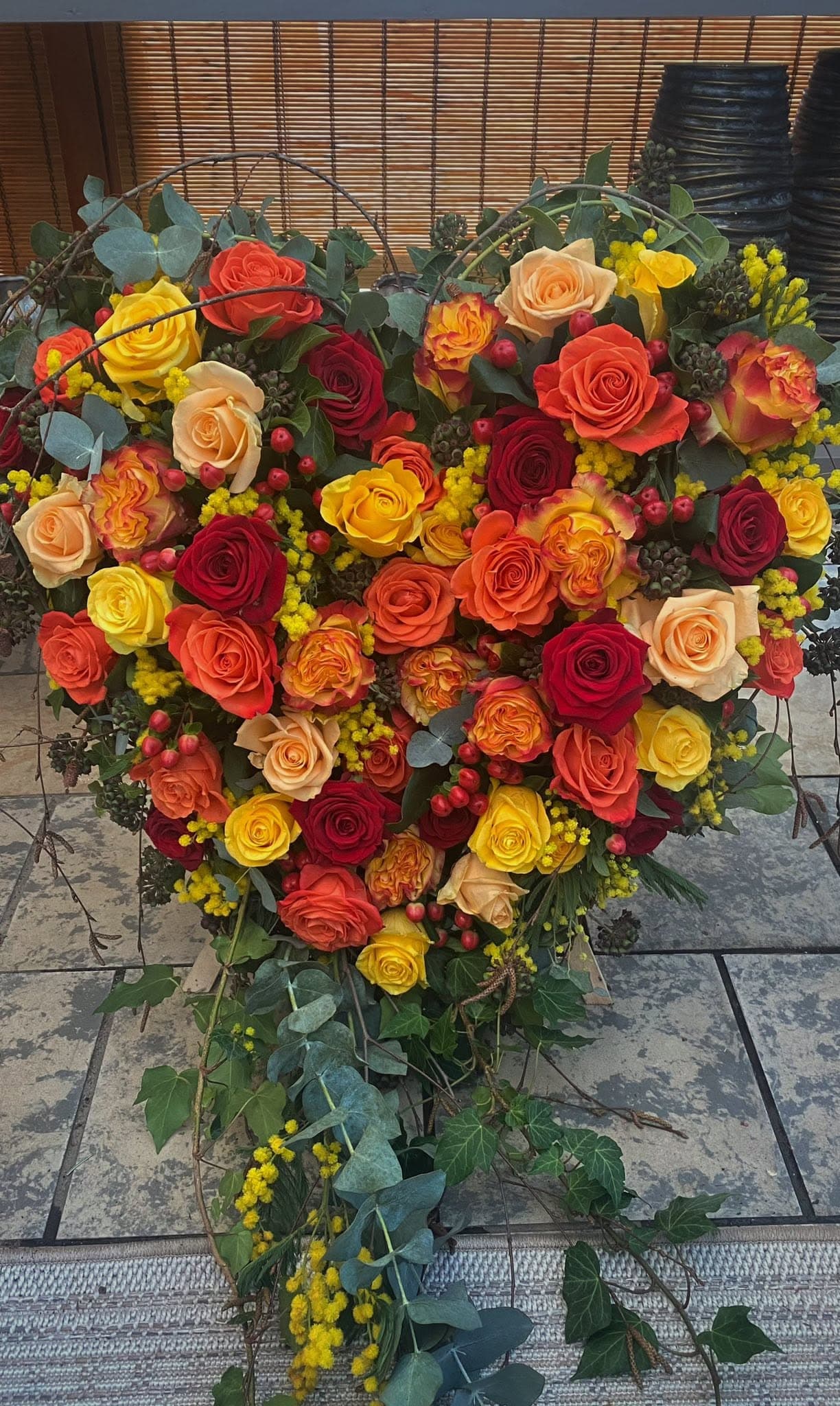 Herzförmiges Trauergesteck aus roten, orangen und gelben Rosen mit Efeu