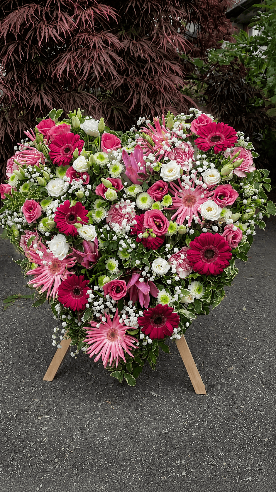 Herzförmiges Trauergesteck aus pinken und weißen Blüten auf einer Staffelei