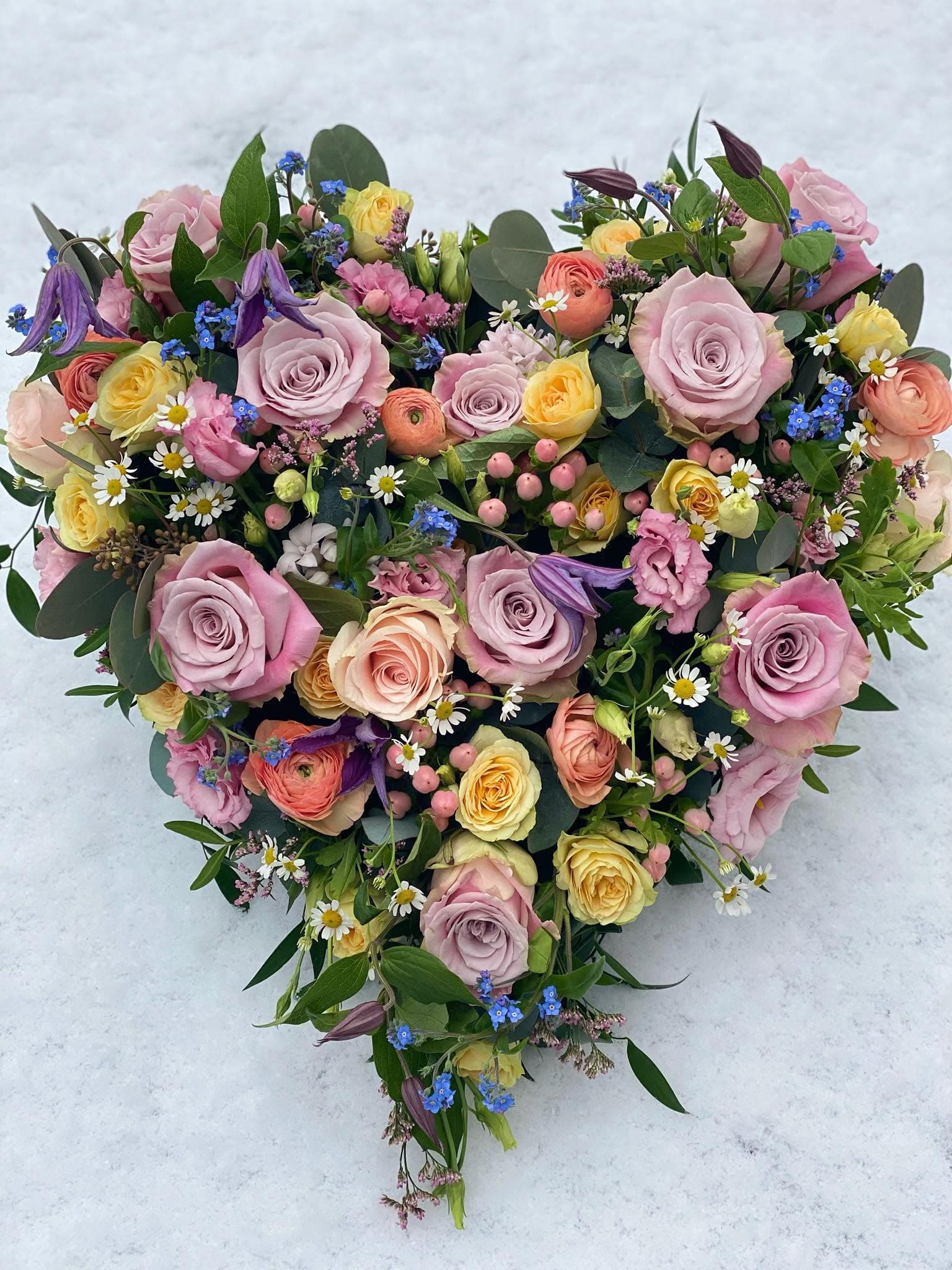 Herzförmiges Gesteck aus rosa Rosen und weißer Kamille auf verschneitem Boden